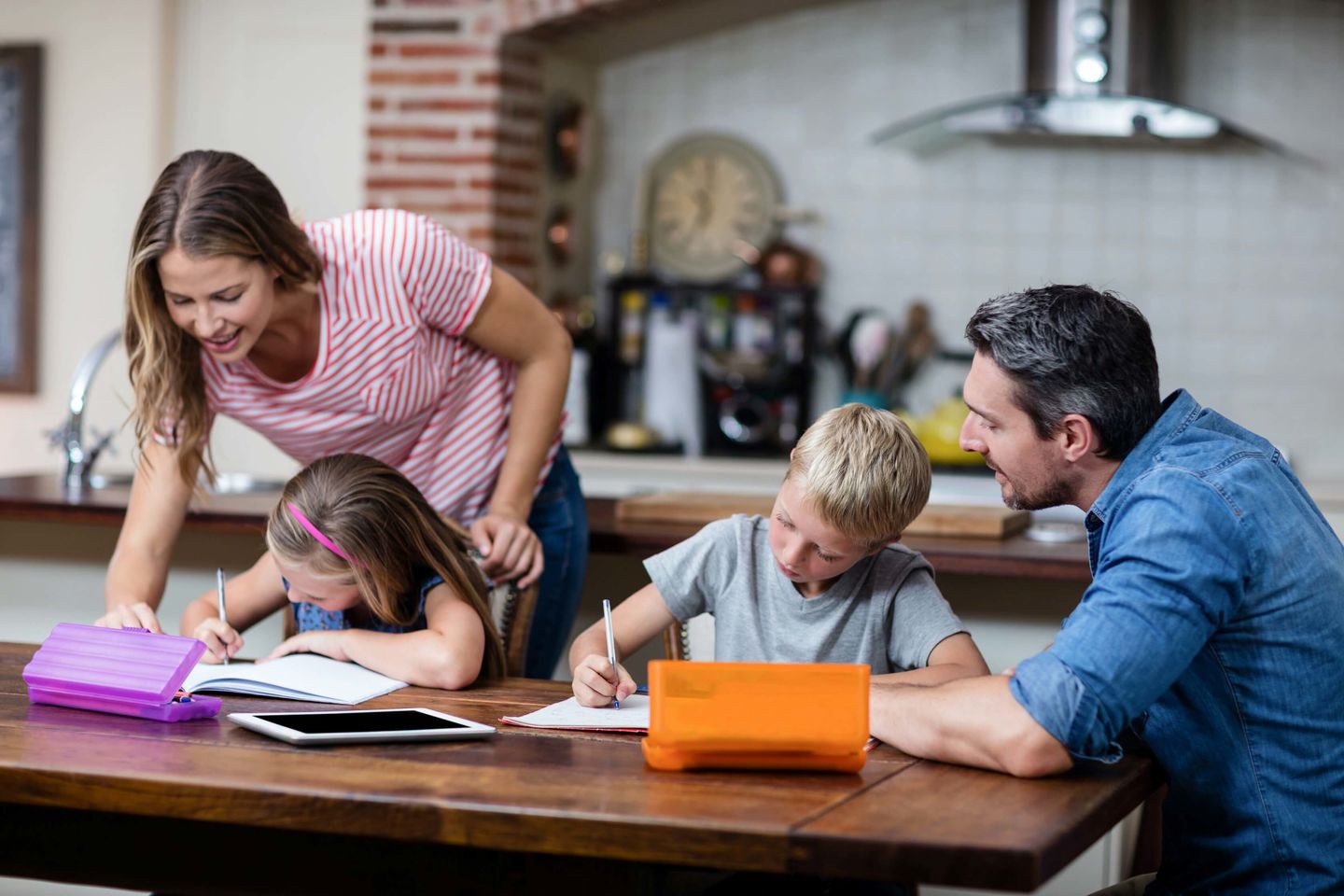 Une mère et un père aident leurs deux jeunes enfants à faire leurs devoirs à table.