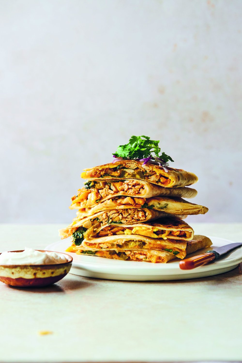 Stack of chicken quesadillas with a side of sour cream